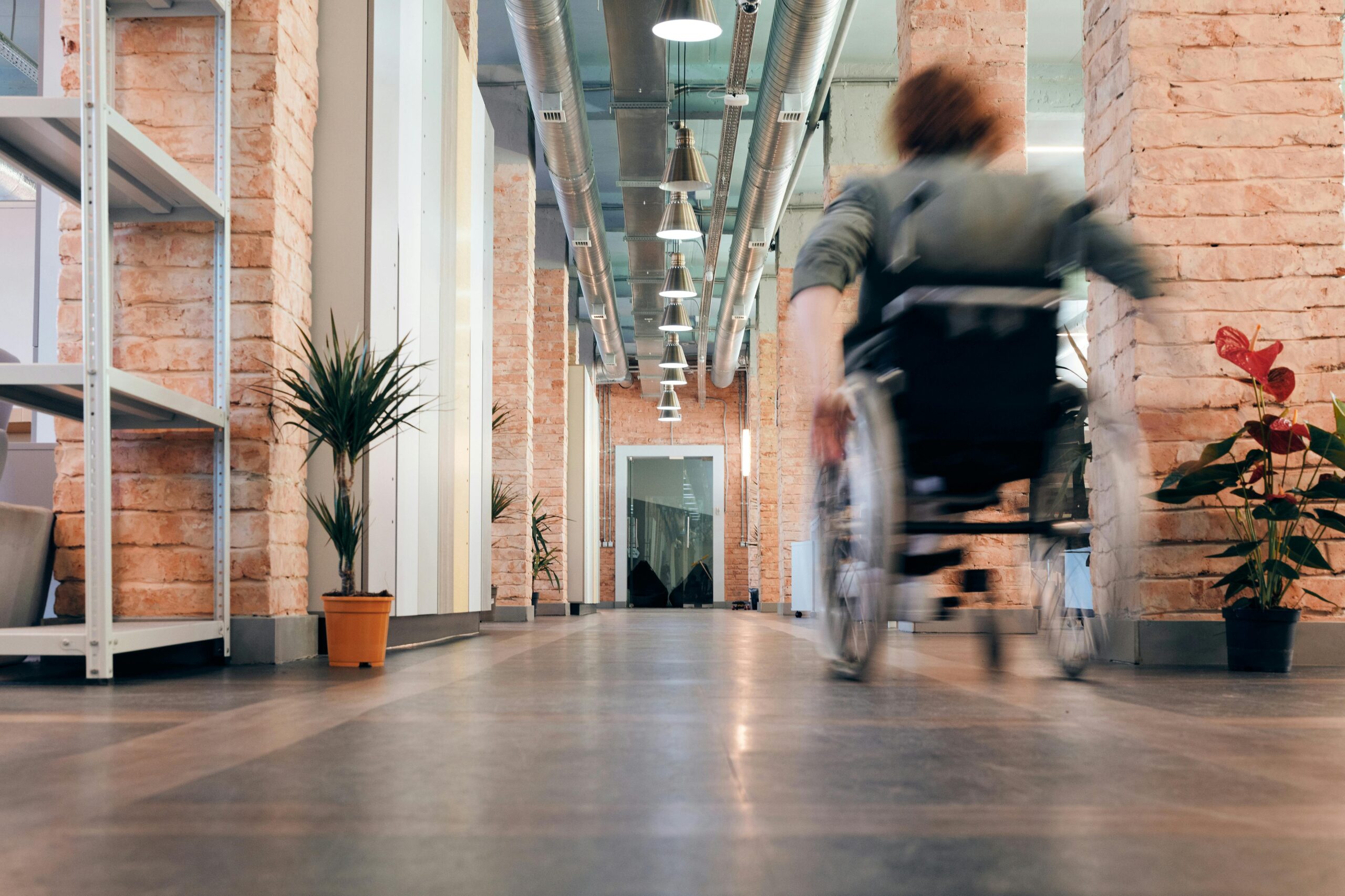 Motion blur of a person in a wheelchair speeding through a modern office hallway with industrial decor.