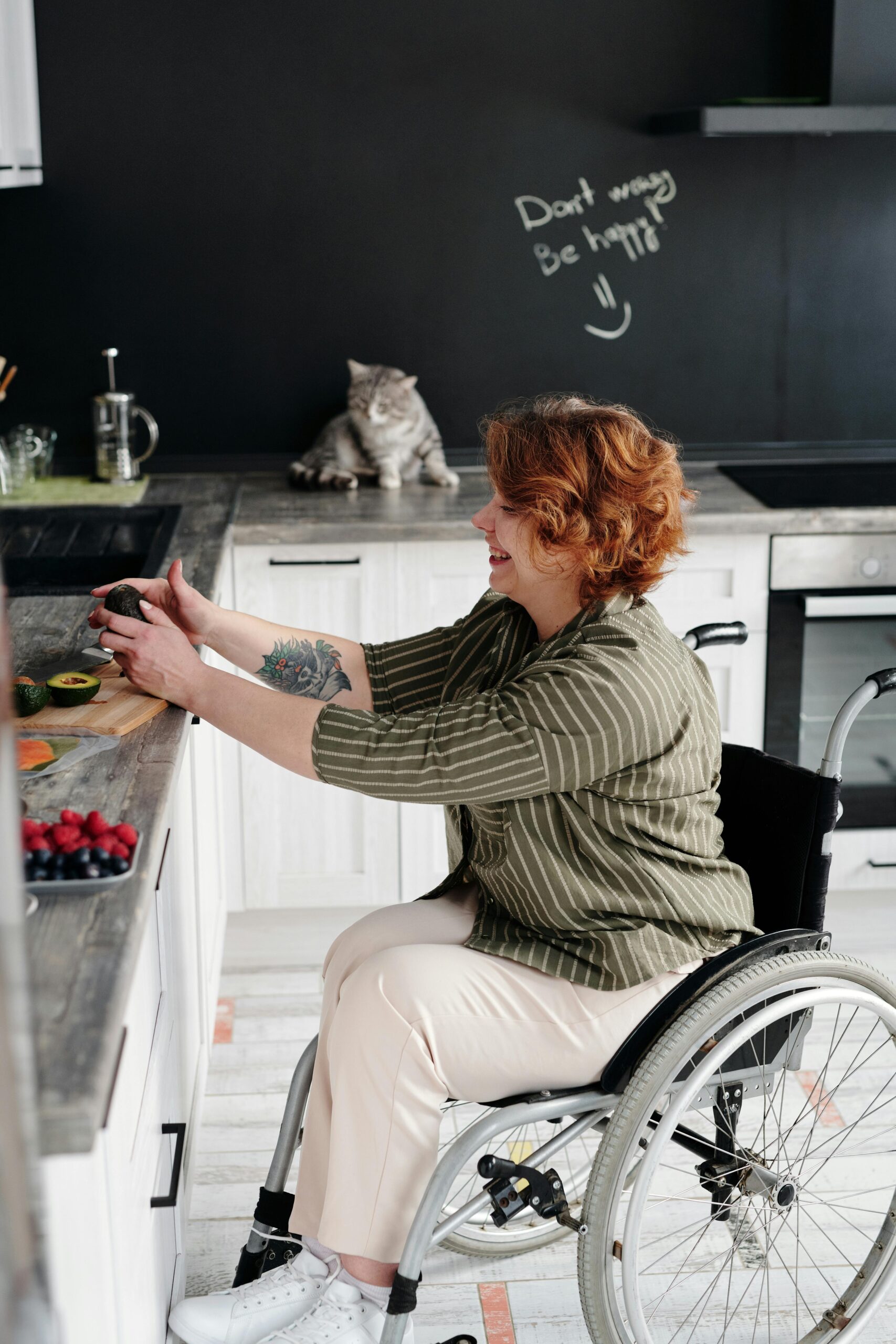 Smiling woman in wheelchair joyfully prepares a healthy avocado meal in her kitchen.