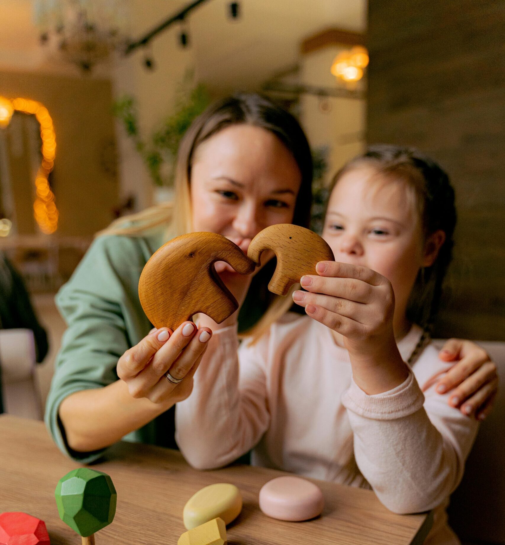 Smiling mother and daughter bonding while playing with wooden toys indoors.